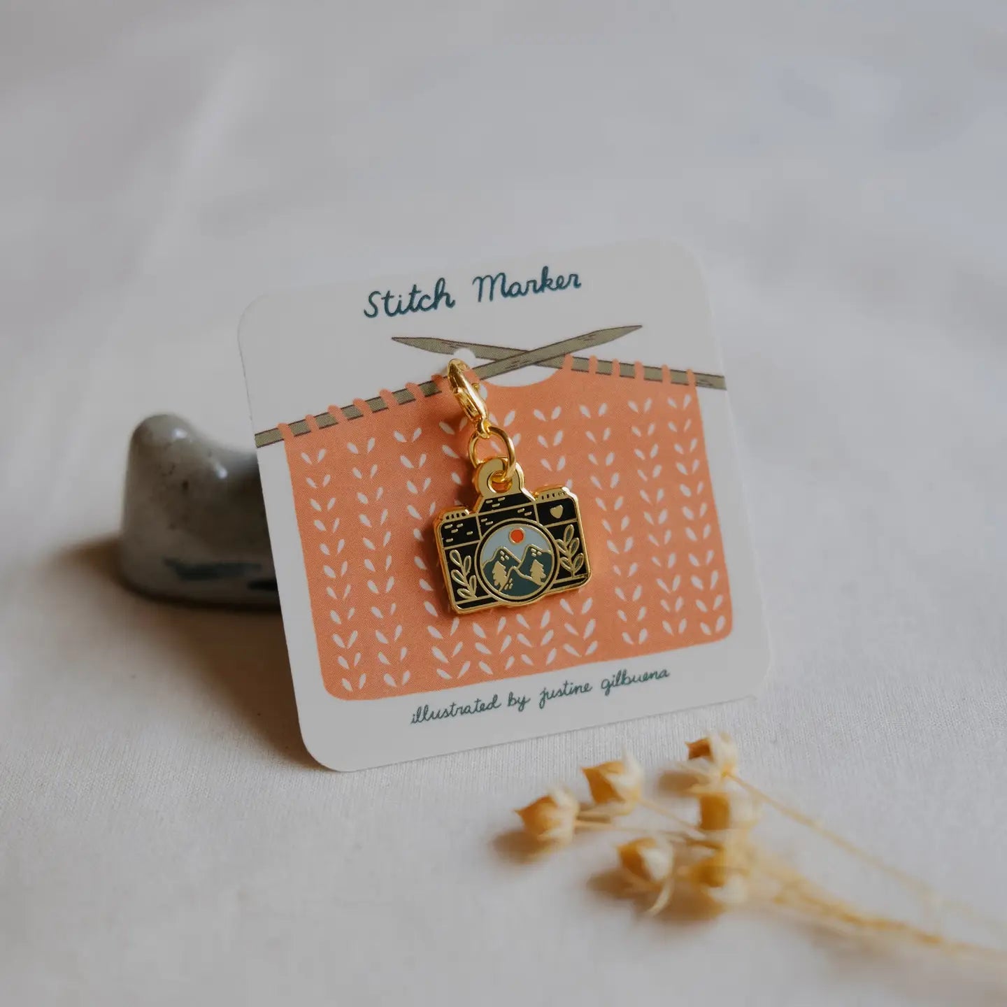 Stitch marker with camera charm on a patterned card with scissors, on a light background