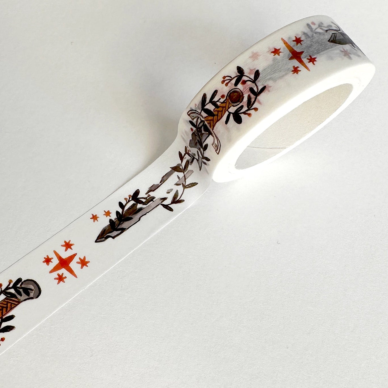 A roll of washi tape with a design that includes swords, shields, and stars in black and red on a white background.