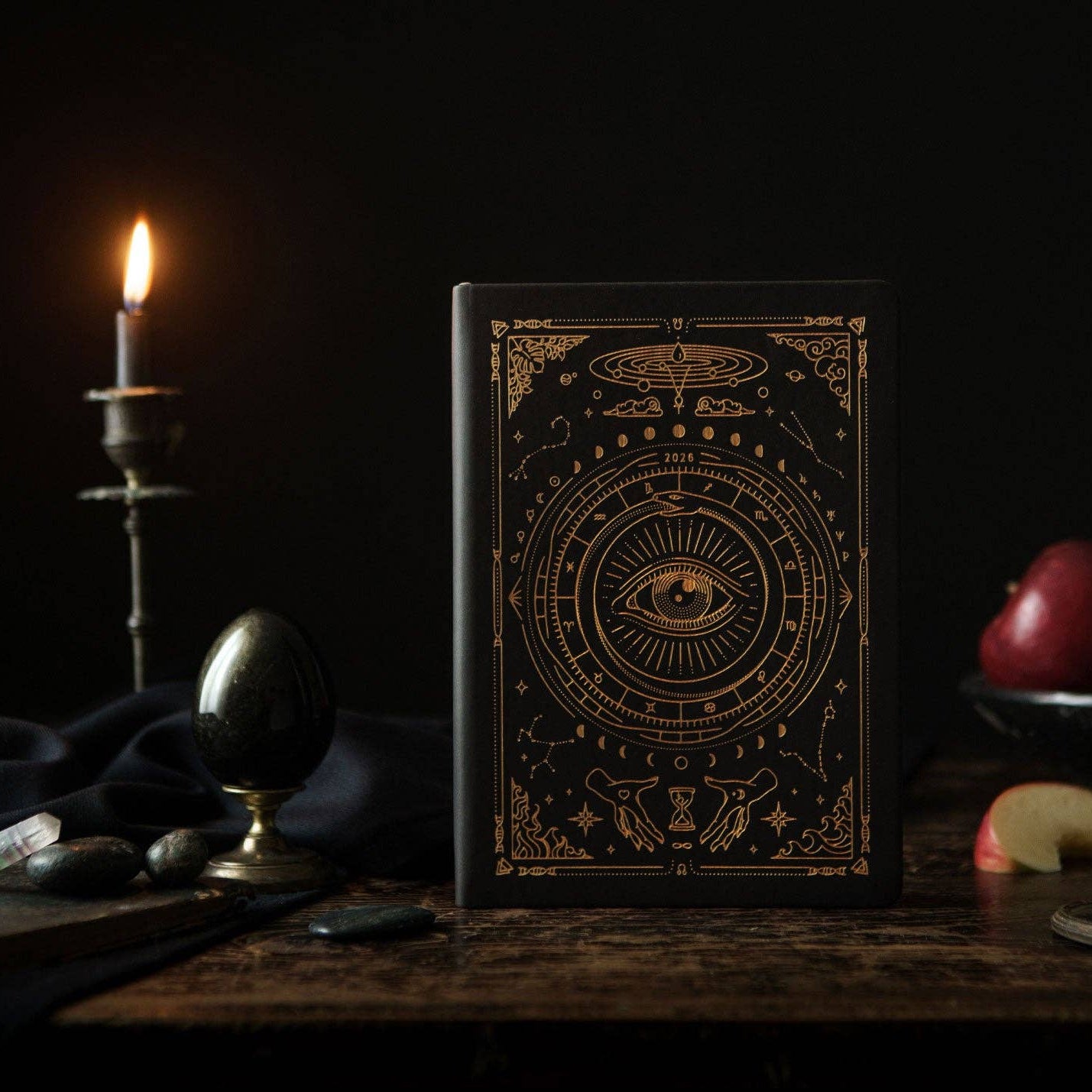 Magic of I - Decorative book with mystical design on a dark wooden table with apples and a candle.