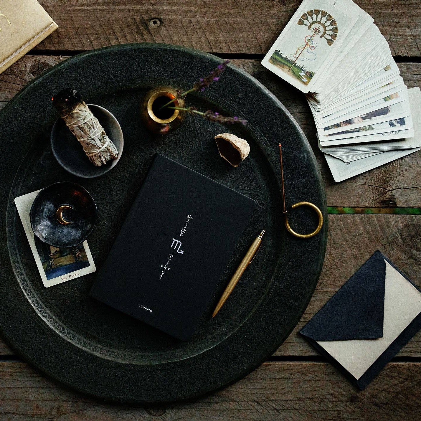 Black book, envelope, and other items on a wooden surface with a dark round tray.
