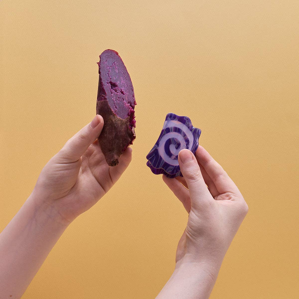 Two hands holding a sliced purple sweet potato against a yellow background