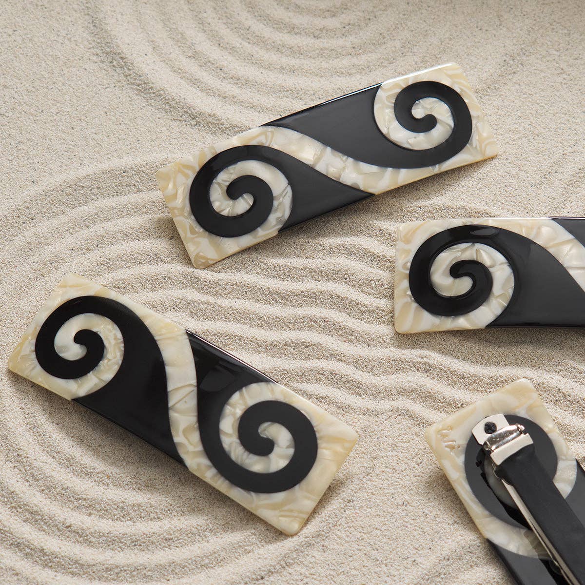 Black and white hair clips with spiral design on a sandy background