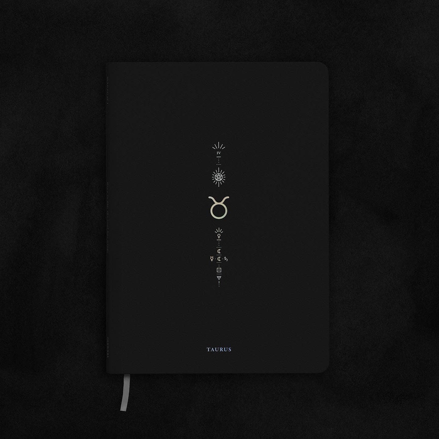 Black notebook with Taurus zodiac symbol on a dark textured background