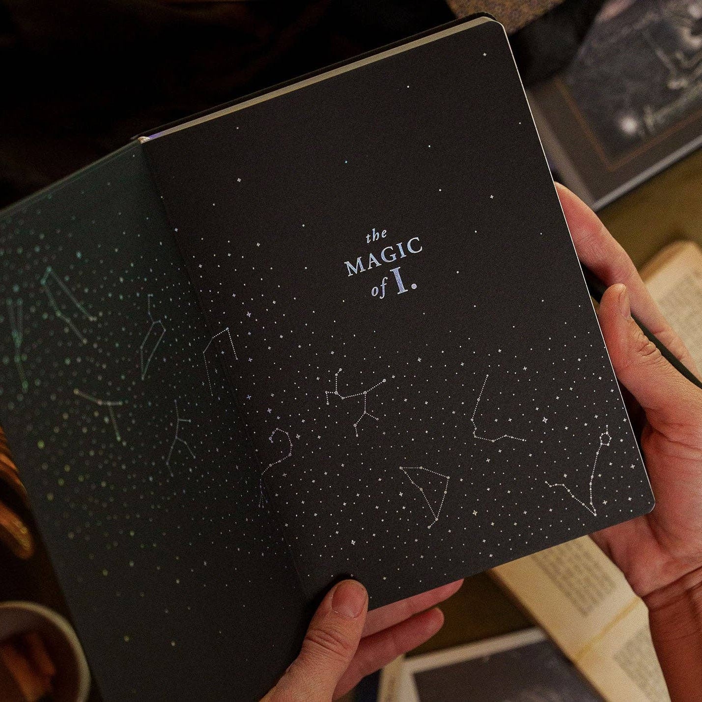 Magic of I - Zodiac Journal - Sagittarius - Black notebook with star constellations and 'the magic of I.' text held by a person.