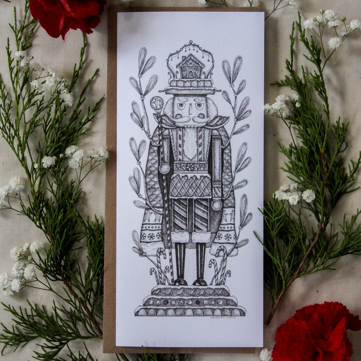 Card with a detailed illustration of a nutcracker surrounded by greenery and red flowers.