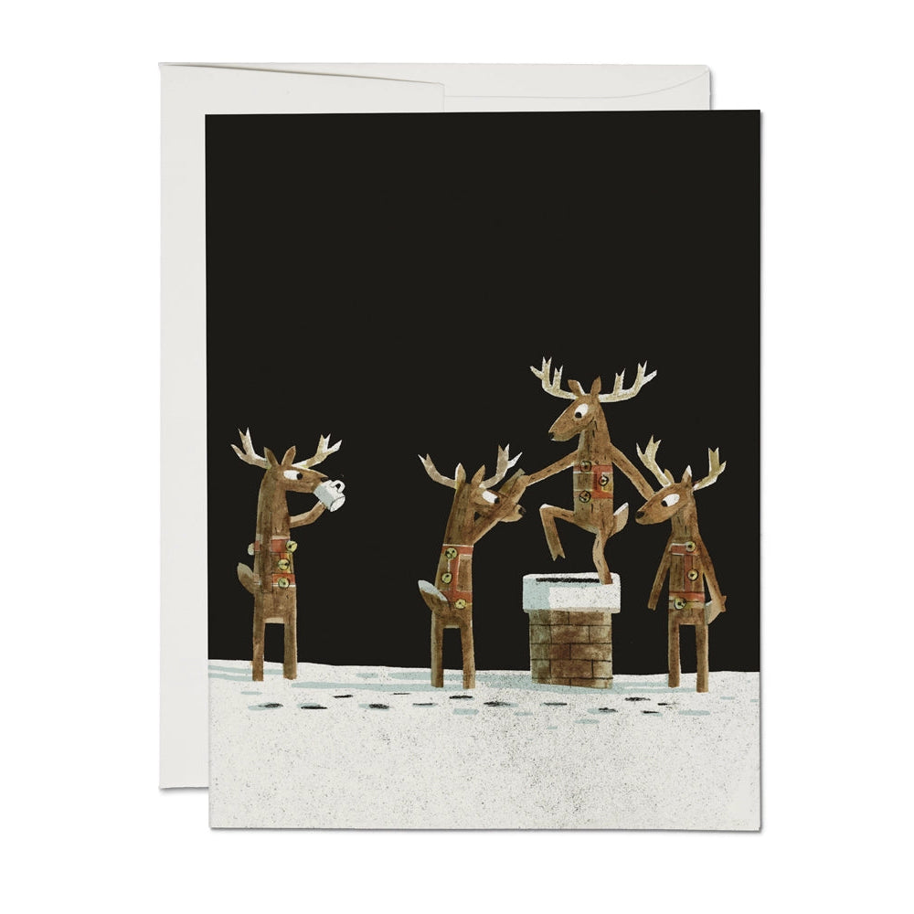 A folded holiday card featuring a group of reindeer with antlers, in brown, black, and white colors, on a snowy background. The card has a blank interior and includes an envelope.