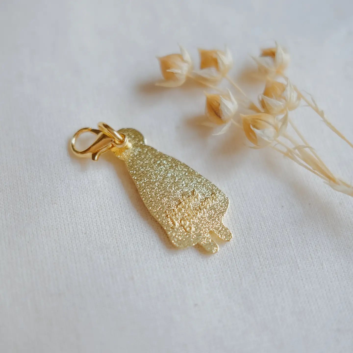 Gold textured pendant on a white background with dried flowers