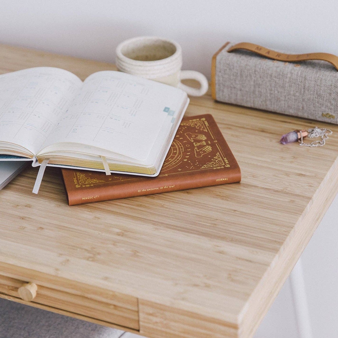 Open book on a wooden desk with a mug and small speaker