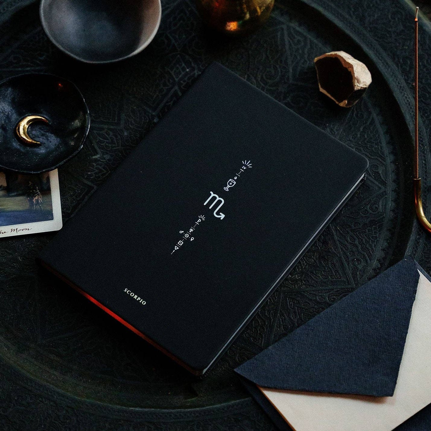 Black notebook with brand logo on a dark surface with decorative items