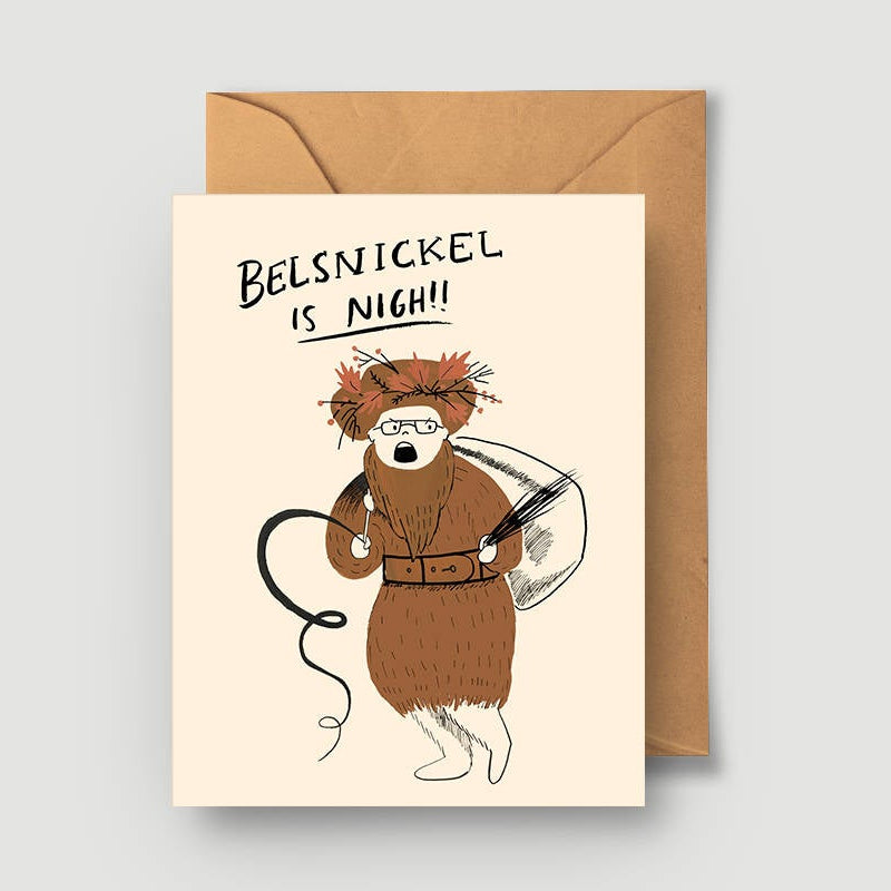 A greeting card featuring an illustration of a character resembling Dwight Schrute from 'The Office', with the text 'Belsnickel Is Nigh!' on it. The card is accompanied by a brown envelope.