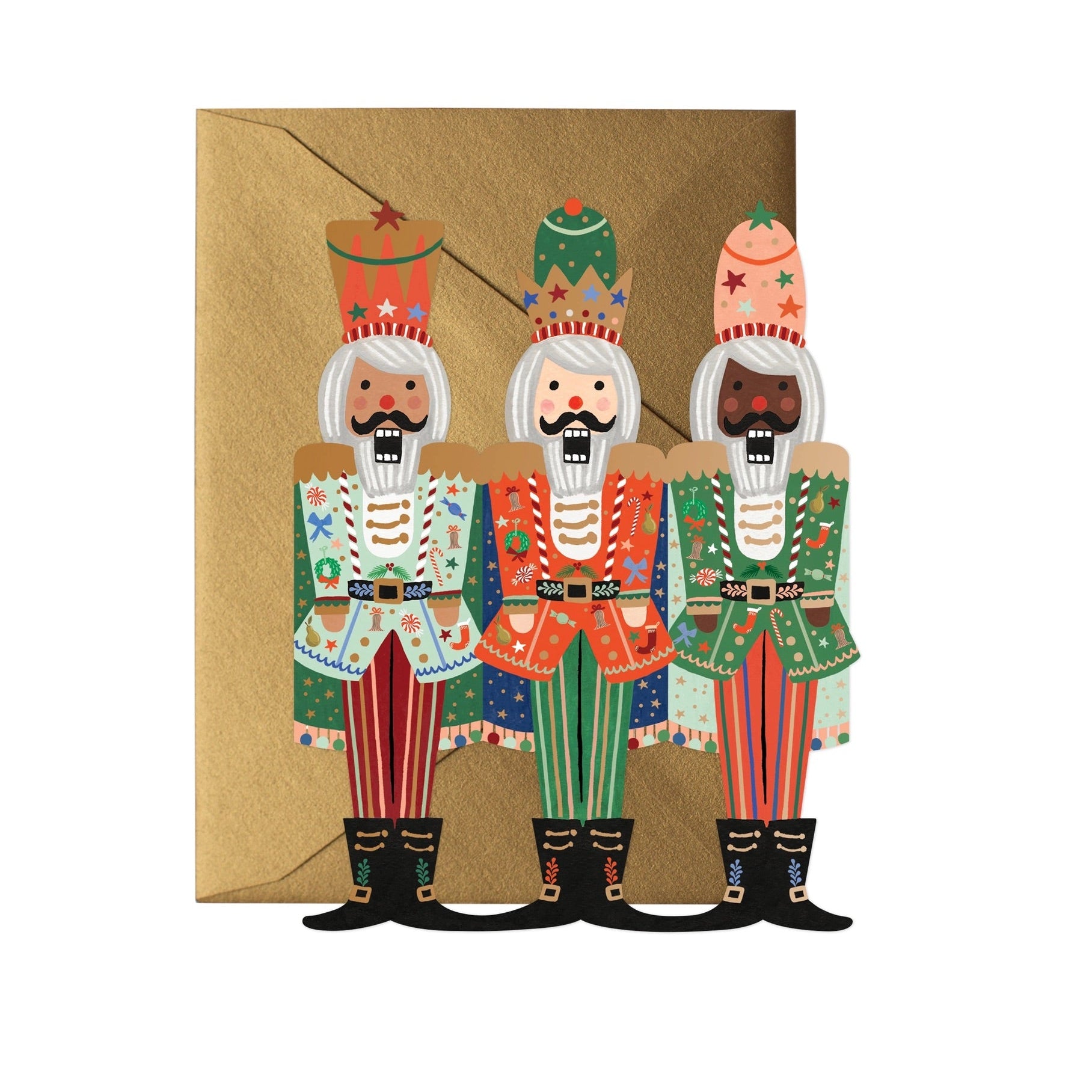A greeting card featuring a die-cut design of three colorful nutcracker figures standing side by side, with a metallic gold foil detail, on a flat surface with a soft white envelope behind it.