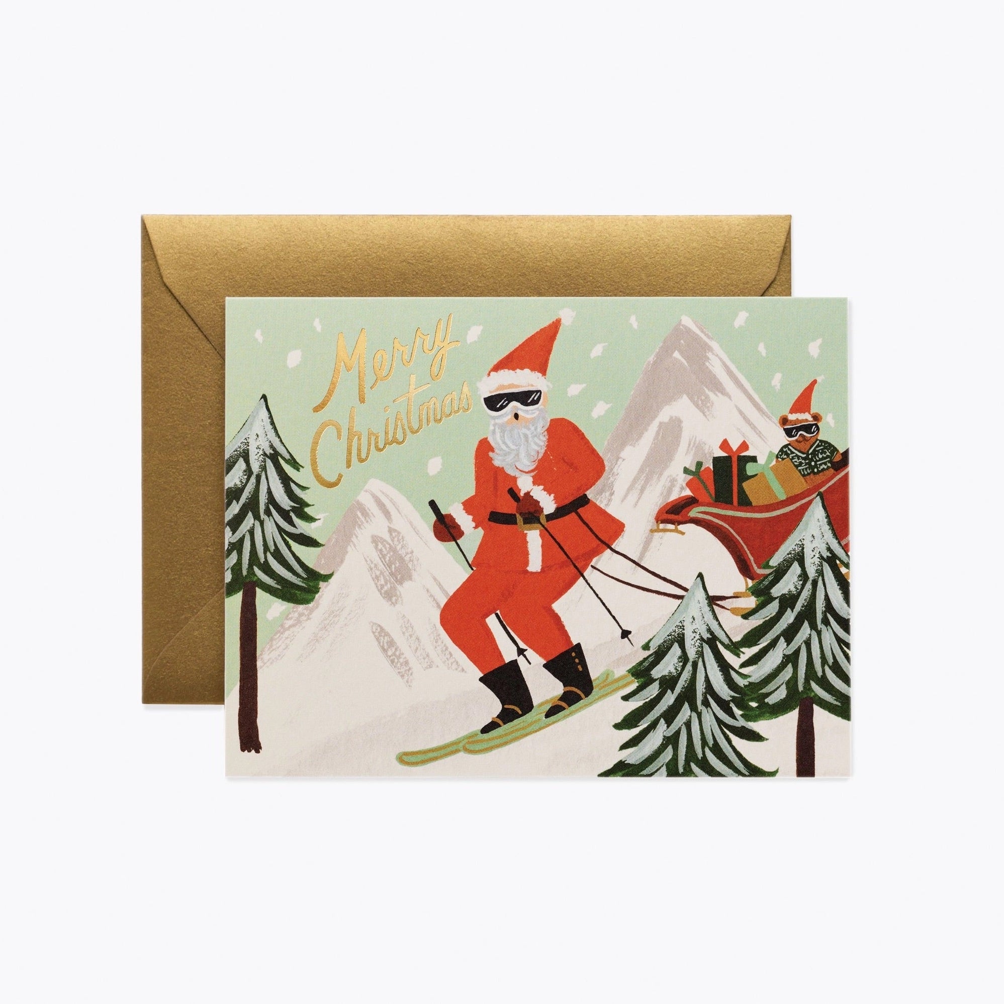 A metallic gold foil card with an illustration of Santa Claus skiing, accompanied by a gold envelope. The card has 'Merry Christmas' and snowflakes in the background.