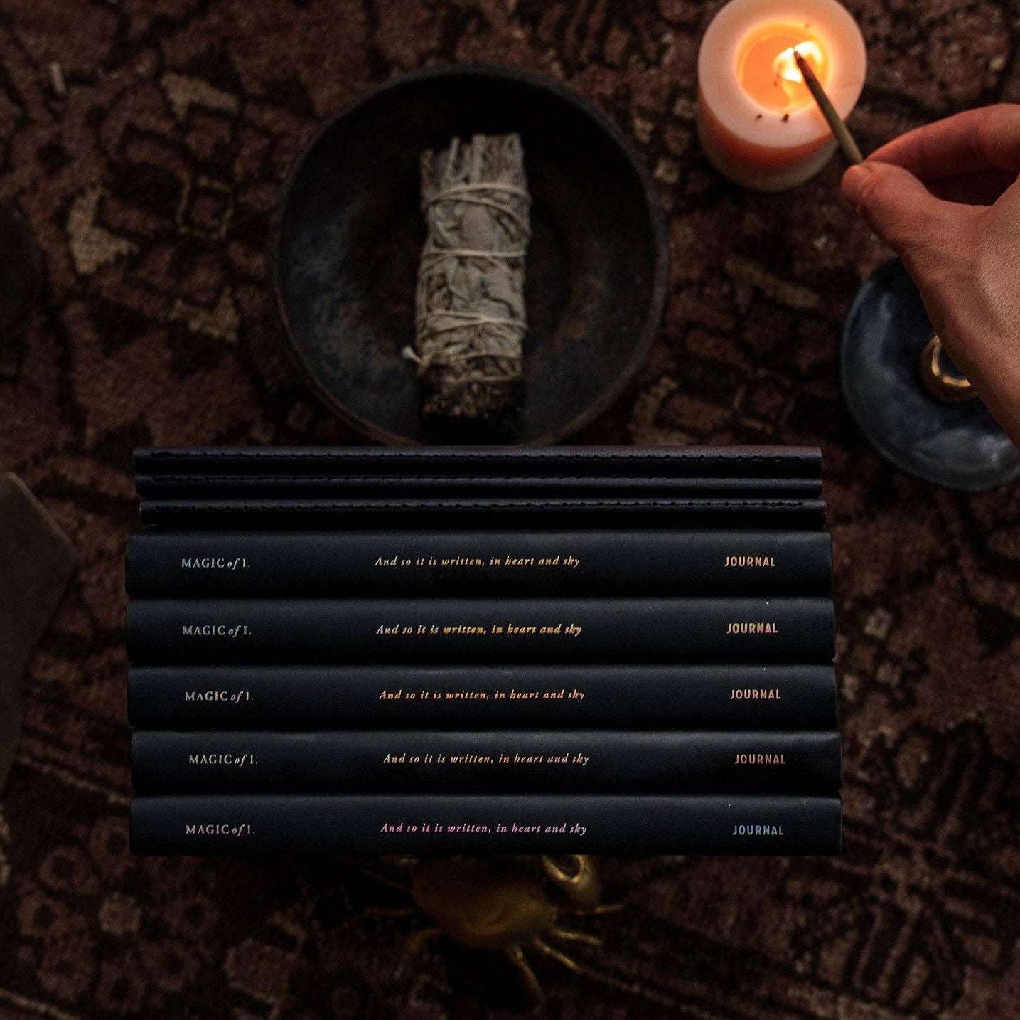Magic of I - Zodiac Journal - Sagittarius - Candle being lit next to a bundle of sage on a textured surface with black books displaying text.