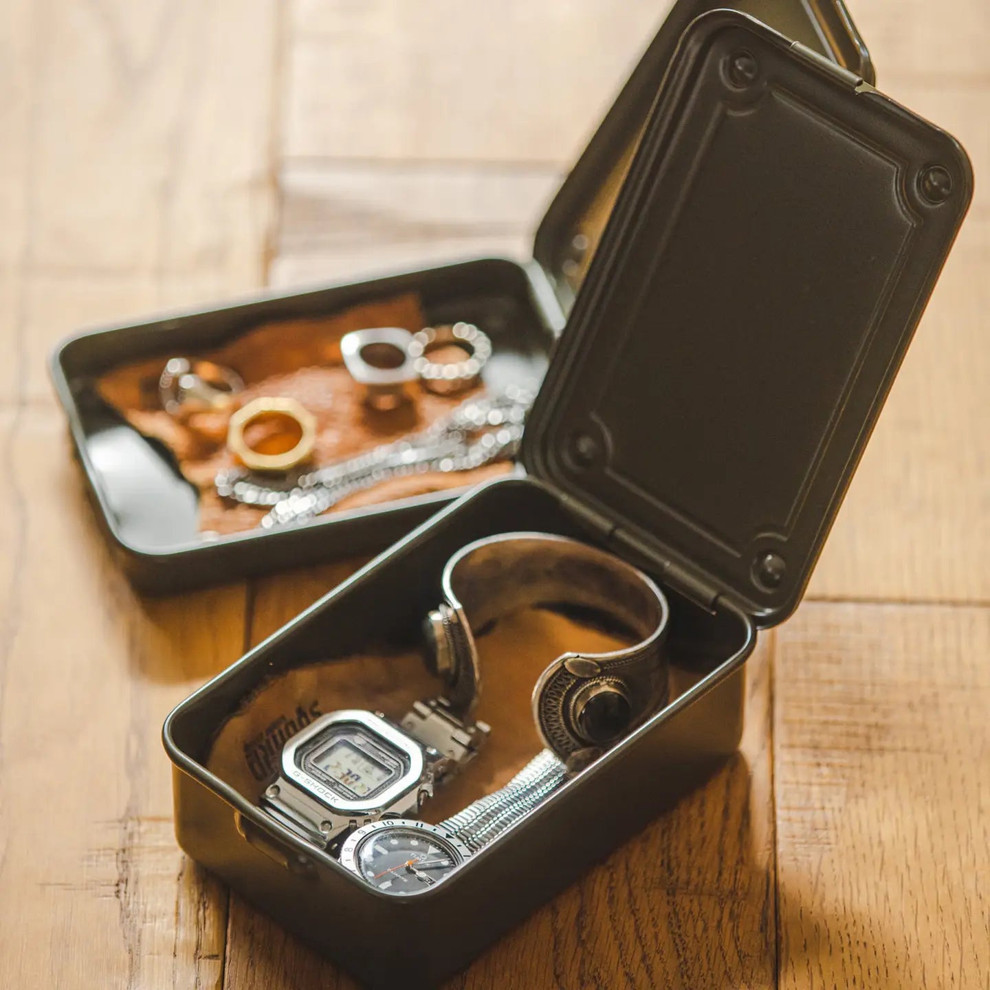 Open black metal box containing jewelry on a wooden surface