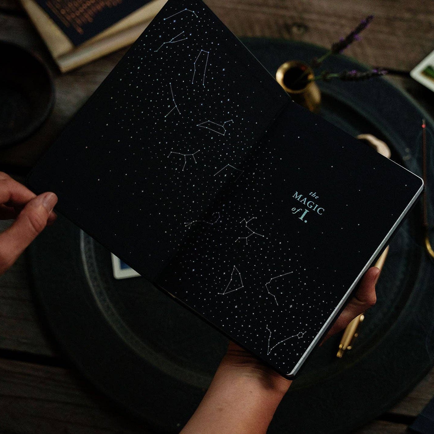 Black notebook with star patterns held by a hand on a wooden surface with books and cards.