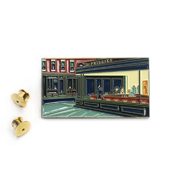 Inspired by Edward Hopper’s “Nighthawks” (1942) this large enamel pin is the perfect statement piece. Nighthawks shows customers sitting at the counter of an all-night diner. The shapes and diagonals are carefully constructed. The viewpoint is cinematic—from the sidewalk, as if the viewer were approaching the restaurant. The diner's harsh electric light sets it apart from the dark night outside, enhancing the mood and subtle emotion.